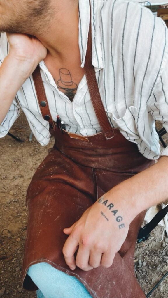 Jonathan sits on a chair. Garage-tattoo on his hand.